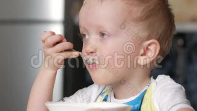 <strong>一个</strong>可爱的金发男孩用<strong>勺子</strong>从房子的盘子里吃粥。 特写
